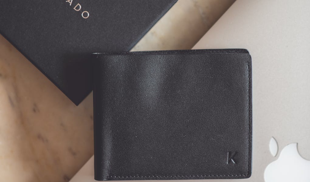 Stylish flat lay showcasing a black leather wallet and modern technology devices on a marble surface.