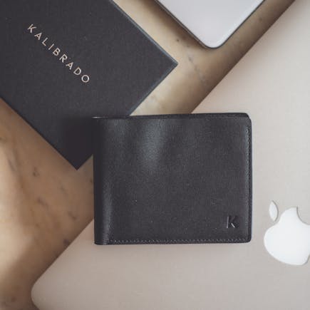 Stylish flat lay showcasing a black leather wallet and modern technology devices on a marble surface.