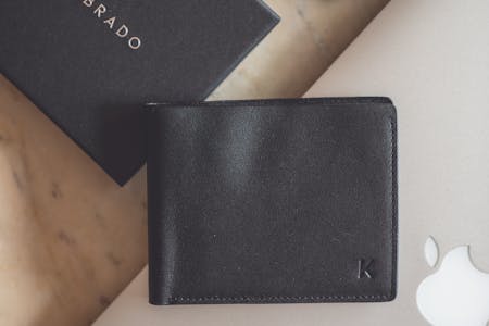 Stylish flat lay showcasing a black leather wallet and modern technology devices on a marble surface.