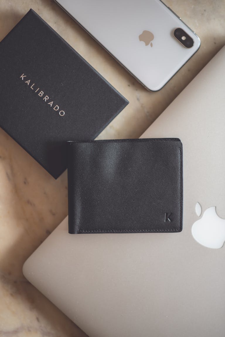 Stylish flat lay showcasing a black leather wallet and modern technology devices on a marble surface.