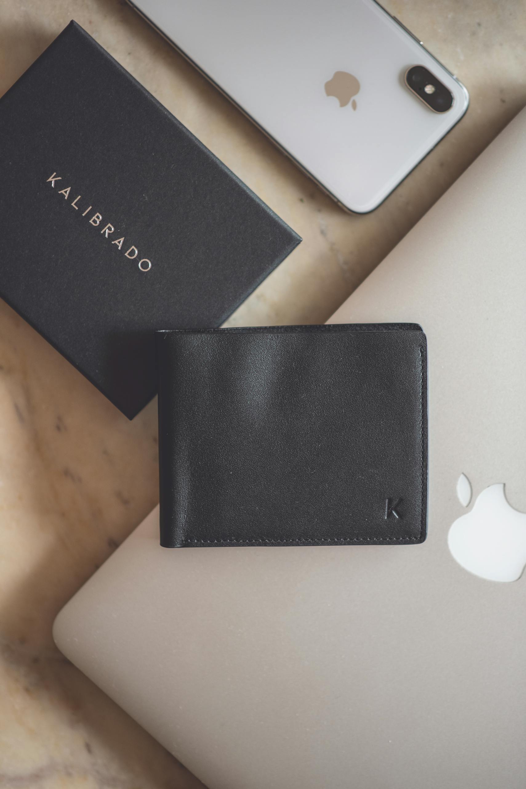 Stylish flat lay showcasing a black leather wallet and modern technology devices on a marble surface.